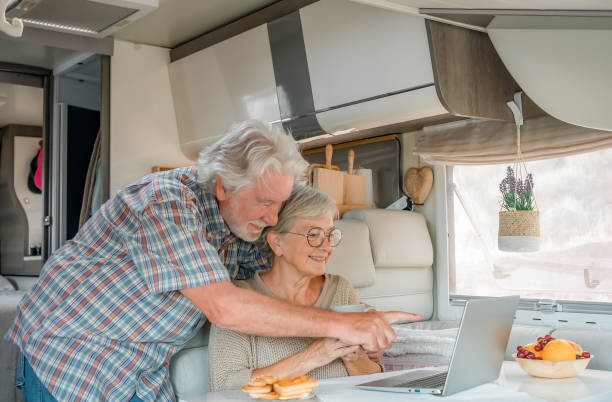 istock Senior beautiful couple in travel vacation inside a camper van browsing on laptop while enjoy breakfast together 1453189695