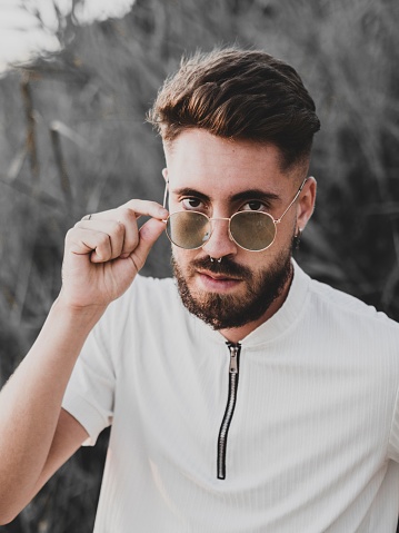A vertical portrait of a Caucasian guy with a beard and sunglasses, looking into the camera