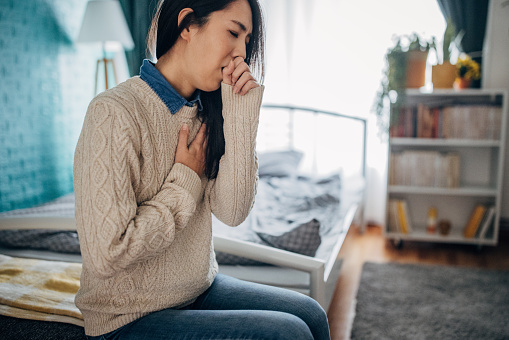 One woman, Japanese woman having chest pain and coughing while sitting in her home.