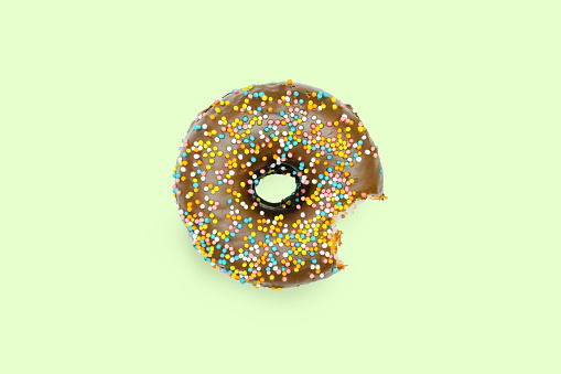 Creative concept of biting eating delicious sweet sugar brown black doughnut donut with glaze on green background. Top view flat lay unhealthy junk dessert, Food concept, mock up, copy space.