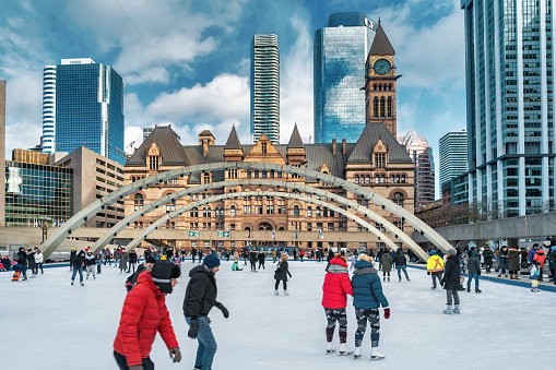 People skate on the Nathan Phillips Square skating rink in downtown Toronto, Ontario, Canada on a sunny winter day.