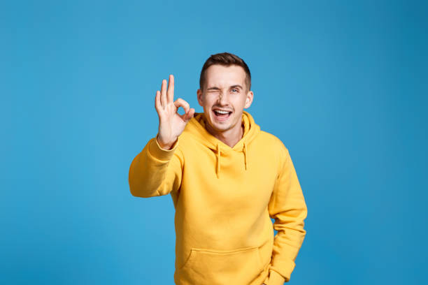 istock young man in yellow sweatshirt showing Ok gesture 1453211144