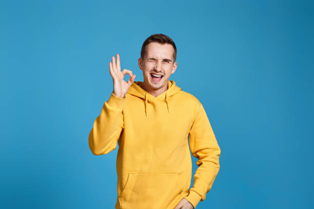 istock young man in yellow sweatshirt showing Ok gesture 1453211145