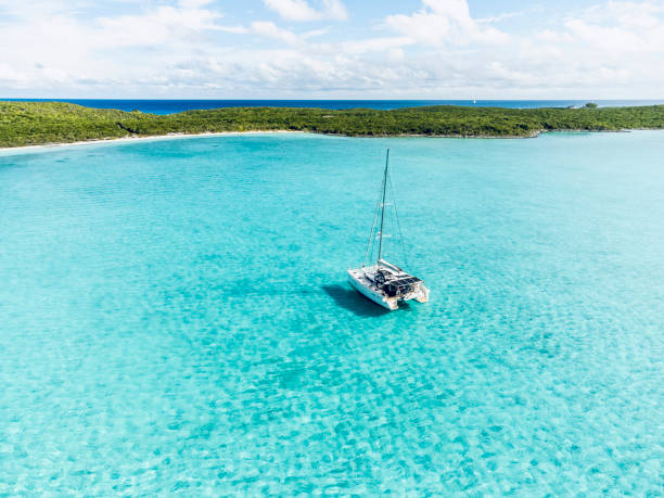 Aerial view of Catamaran anchored in turqoise waters at Musha Cay, Exuma Sailing catamaran on anchorage in coral waters in Bahamas exuma stock pictures, royalty-free photos & images