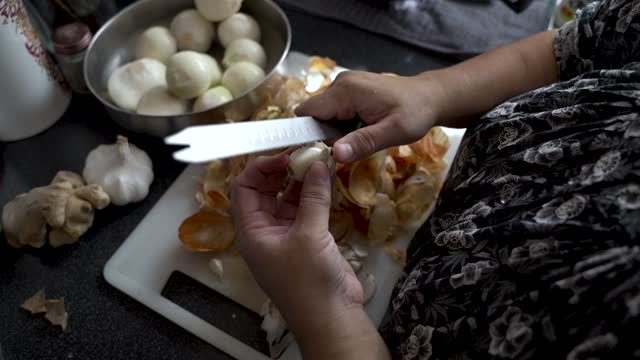 Over Shoulder View Of Hands Peeling Garlic Cloves With Bread Knife. Slow Motion