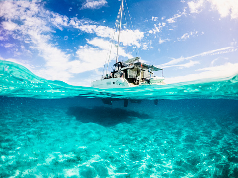 Picture parted in half above and half underwater image of Lagoon Catamaran anchored in Musha Cay, Exuma, Bahamas