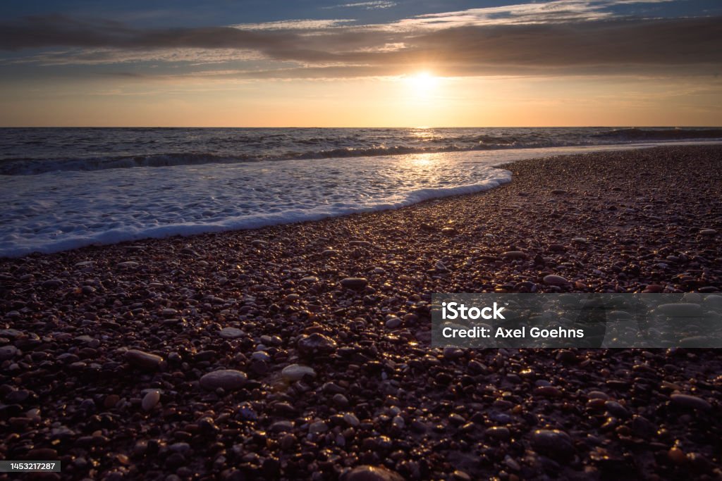 Sunset on beach with small stones in foreground With waves on sea Beach Stock Photo