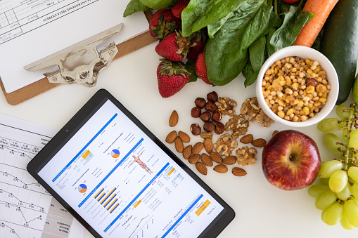 Closeup of nutritionist's desk with healthy food and digital tablet showing body mass index measurement report and nutritional plan - Buenos Aires - Argentina