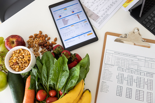 Closeup of nutritionist's desk with healthy food and digital tablet showing body mass index measurement report and nutritional plan - Buenos Aires - Argentina
