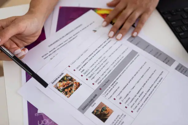 Photo of Close up of hands of a female nutricionist doctor and deportologist in her desk's office during a medical consultation pointing out a diet plan