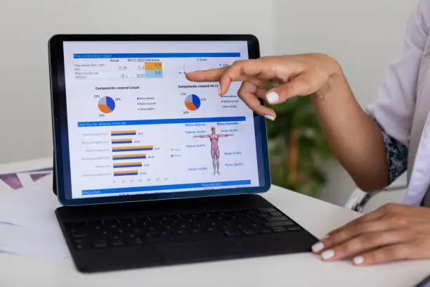 Photo of Close up of hands of a female nutricionist doctor and deportologist  pointing out  a document in her computer during a medical consultation