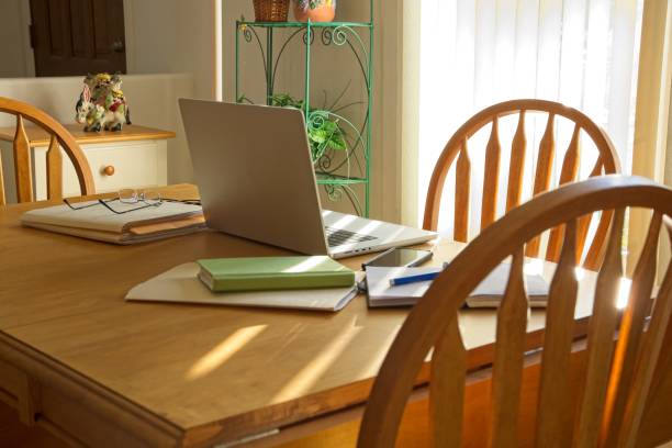 istock Working from home concept at sunny dining room table with laptop surrounded by paper files and notebooks. 1453230706