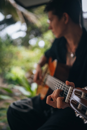 Photo of a young man playing guitar on a balcony surrounded by tropical trees