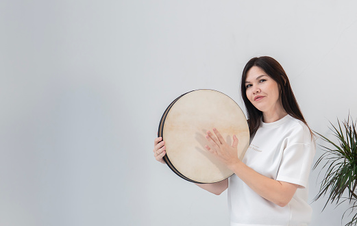 A young woman, a brunette with long hair, holds a tambourine (ocean drum) in her hands