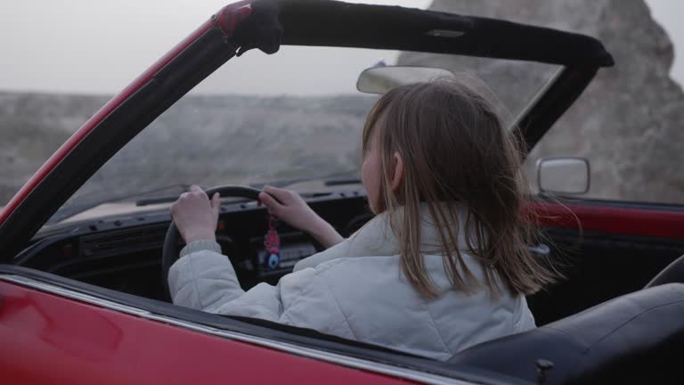 Young woman in red convertible car is touching a steering wheel in mountains.