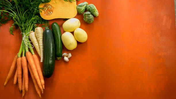 Fresh vegetables, carrots, potatoes and squash on an orange surface