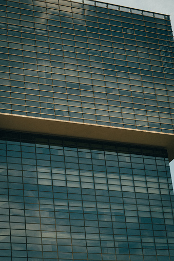 Abstract fragment of modern architecture, walls made of glass and steel. Blue cloudy sky reflections
