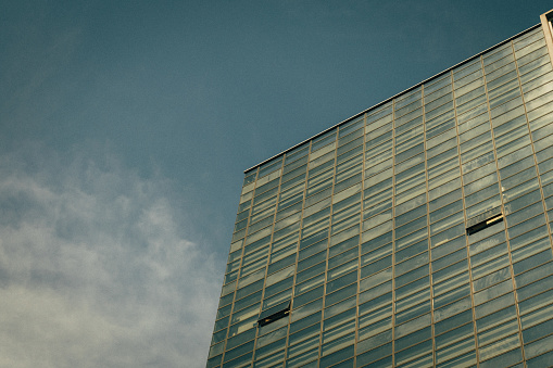 Abstract fragment of modern architecture, walls made of glass and steel. Blue cloudy sky reflections