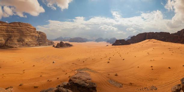 Panoramic view of Wadi Rum desert in Jordan with clouds moving over flat sand landscape with mountains in background, stock photo