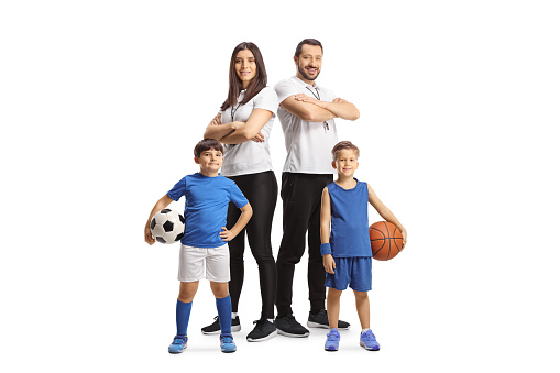 Boys holding basketball and football in front of a male and female trainers isolated on white background