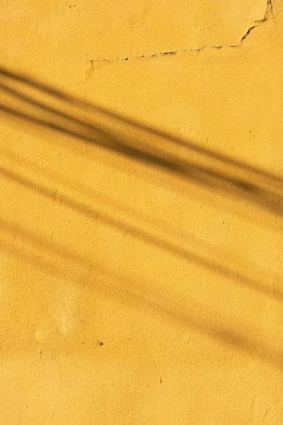 istock Vertical shot of a yellow cracked wall with shadows casting on it 1453257405