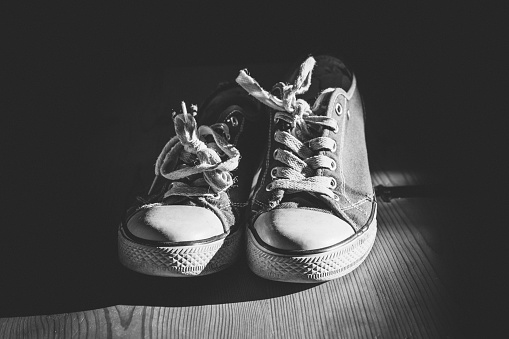 A grayscale shot of an old chuck sneakers on a wooden surface with dark background