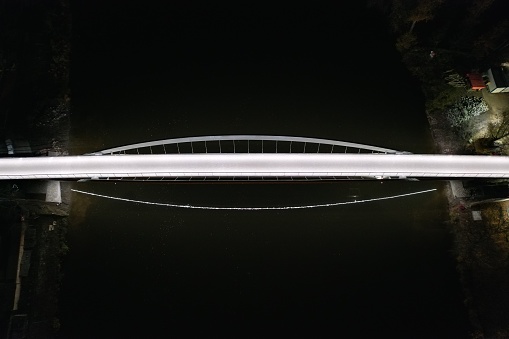 A top view of a pedestrian bridge illuminated in white light across the Elbe River in Nymburk at night