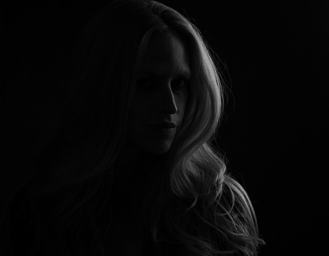 A young blonde female with dramatic and mysterious side of the face in black and white