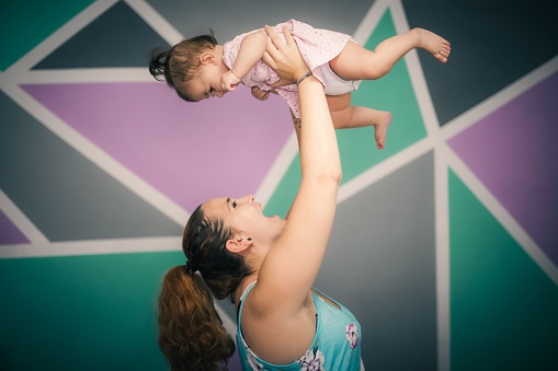 A portrait of a mother playing with her little girl with colorful wall in the background