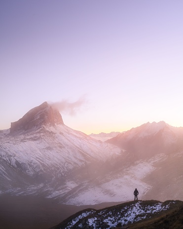 A vertical shot of a man silhouette in front of a foggy and snowy mountain range at sunset in Col du Sanetsch, Switzerland