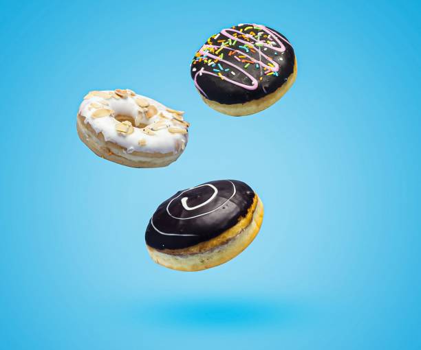 istock Chocolate and vanilla sweet donuts with sprinkles flying over blue background 1453268241