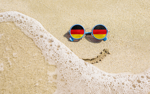 Sunglasses with flag of Germany on a sandy beach. Travel and vacation concept for Germans