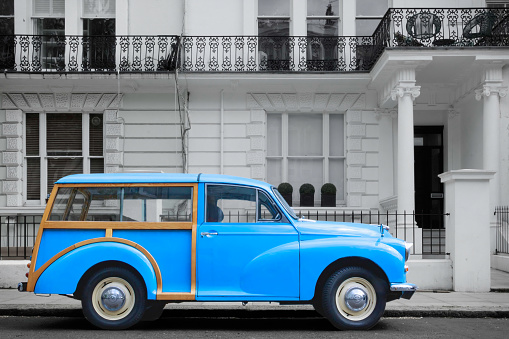 British blue vintage station wagon with wooden frame and chrome accessories from the 1950s or 1960s in front of white plastered Victorian facades with classical Renaissance pillars and cast iron railings, London, United Kingdorm. High quality photo