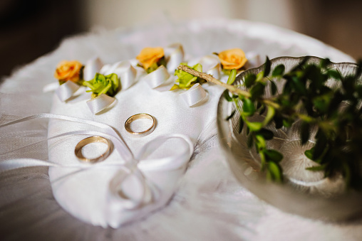 Two golden wedding rings of the bride and groom, close-up on a heart-shaped pillow in the church on the table