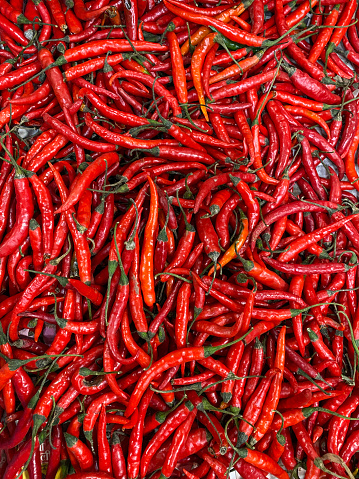 Stock photo showing glossy red chilli peppers spread out to be sold at an outdoor fruit and vegetable market.