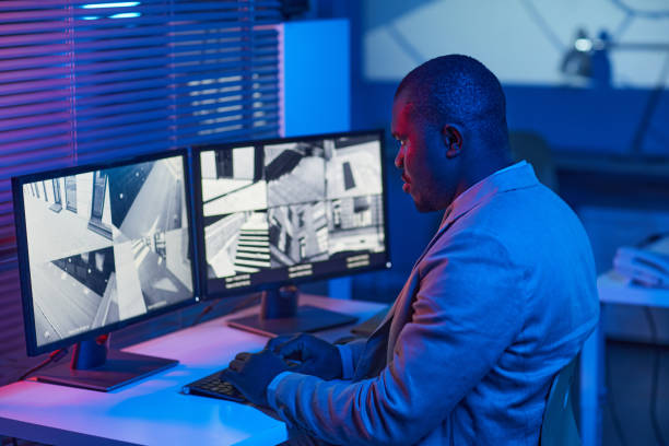istock Black man looking at surveillance camera footage in security center office 1453276516
