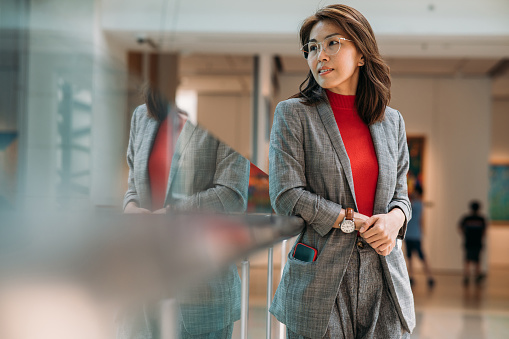 Confident smiling Asian businesswoman standing by window in office.