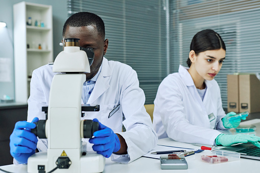 top view of scientists in uniforms looking through microscopes in laboratory