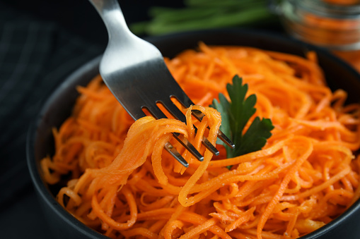 Fork with Korean carrot salad over bowl, closeup