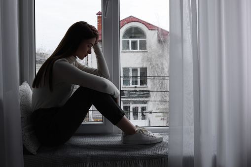 Unhappy young woman near window indoors, space for text. Loneliness concept