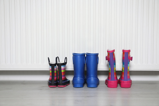 Different pairs of boots near modern radiator indoors