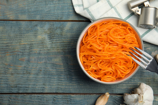 Delicious Korean carrot salad and garlic on blue wooden table, flat lay. Space for text