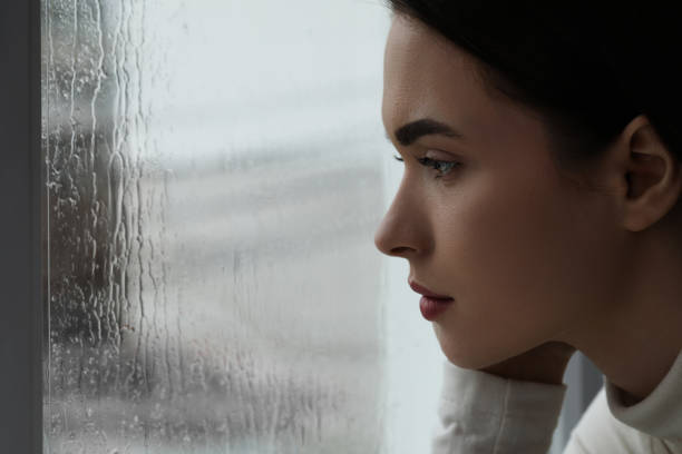 меланхоличная молодая женщина наблюдает за дождем через окно, крупным планом с пространством для текста. концепция одиночества - pessimistic стоковые фото и изображения