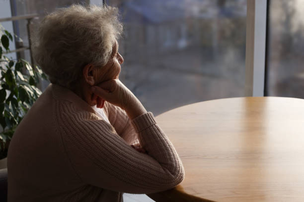anciana mirando por la ventana en un día lluvioso, espacio para el texto. concepto de soledad - pessimist women one person caucasian fotografías e imágenes de stock