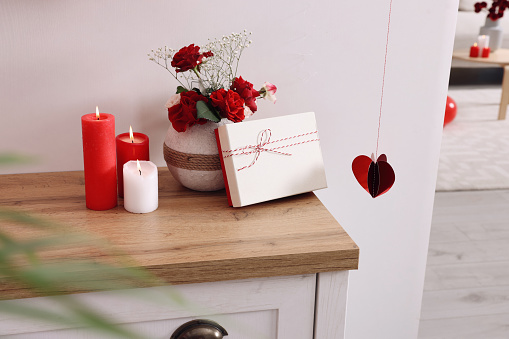 Vase with beautiful flowers, gift box and candles on wooden table indoors. Happy Valentine's Day