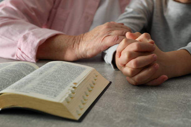 istock Boy and his godparent praying together at grey table, closeup 1453280204