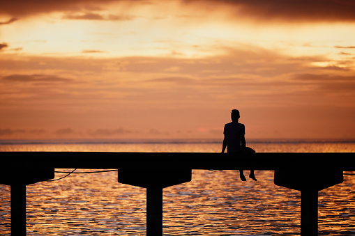 Man thinking on edge of pier and looking at ocean at golden sunset.