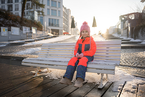 Portrait of Caucasian girl in warm clothing sitting on a bench in the city, during sunny winter day