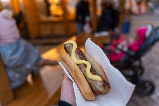 POV of unrecognizable man holding bun with sausage, at the Christmas market