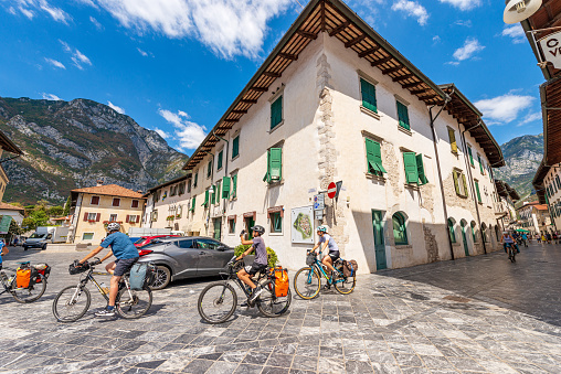 Venzone, Italy - August 11, 2022: Ancient town hall square (Piazza Municipio) in the small village of Venzone, partially destroyed by the 1976 earthquake and rebuilt between 1979 and 1984. Udine province, Friuli-Venezia Giulia, Italy, Europe. A small group of cyclists cross the ancient square on a sunny summer day.